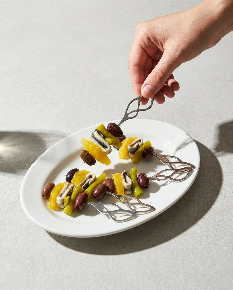 Mano sirviendo un pincho de gilda con naranja en una brocheta metálica de curvas