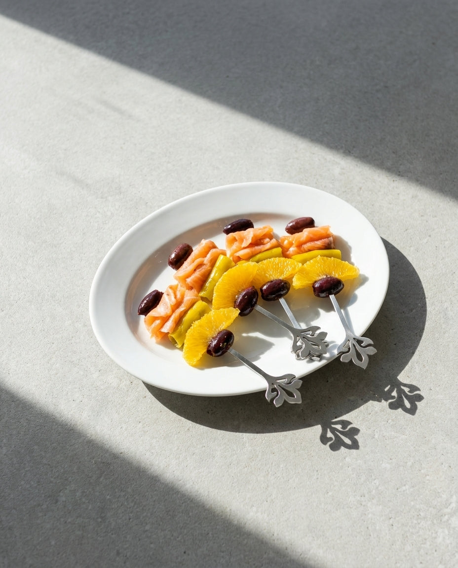 Juego de cuatro brochetas metálicas con diseño de flor presentando gildas gourmet de salmón, naranja y aceituna negra en un plato